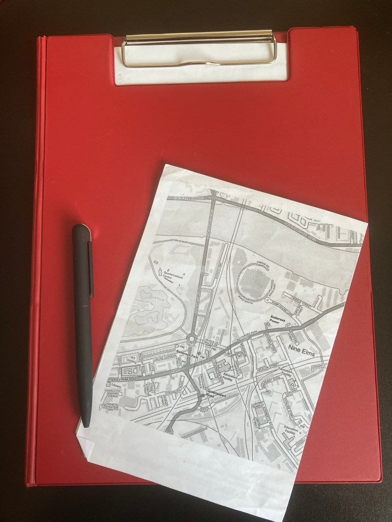 A red clipboard with part of a map of Nine Elms on top of it and a black pen