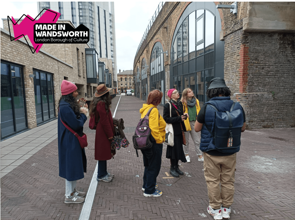 A group of people standing on a brick path looking up at a Victorian railway viaduct. 