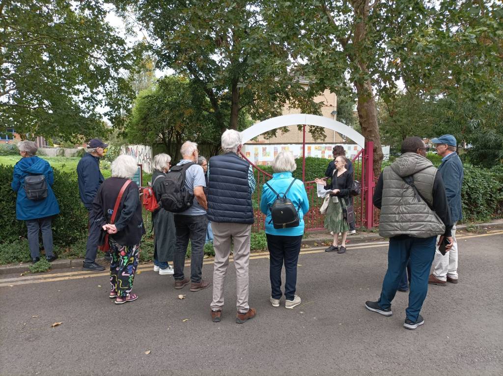 A group of people standing in a semi-circle in front of a fenced off grass area.